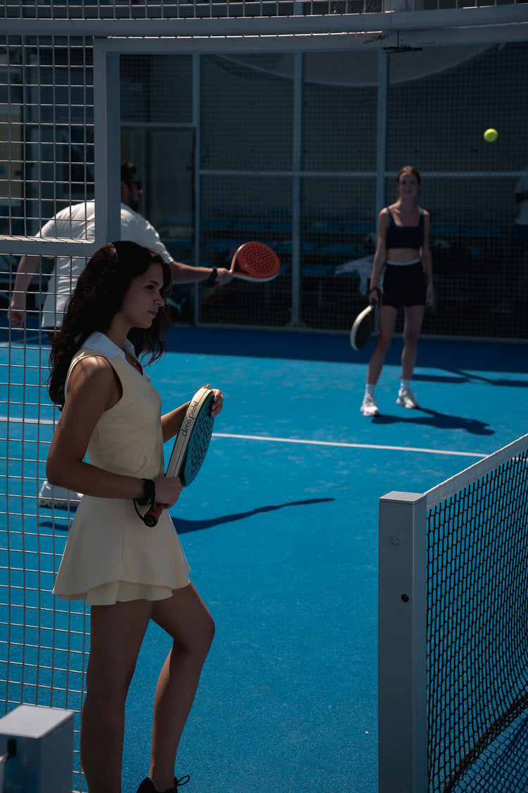 Player in a cream tennis dress holding a green Clima racket on court