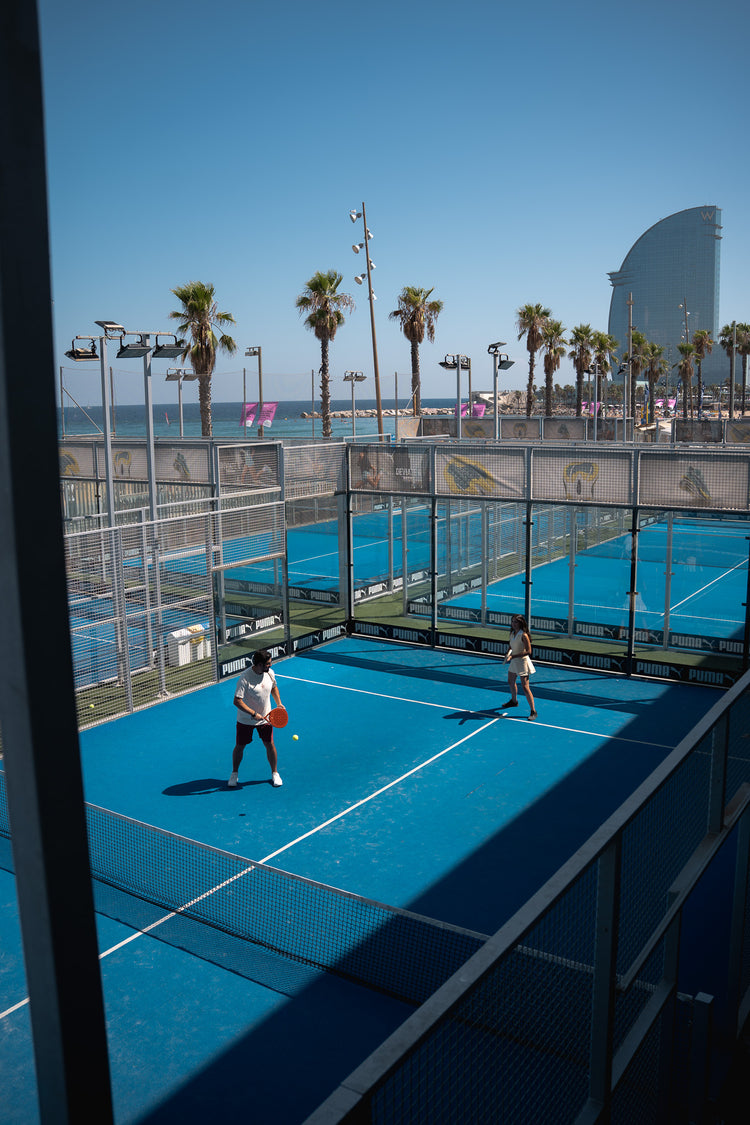Doubles on a blue beach court with palms and the sea behind