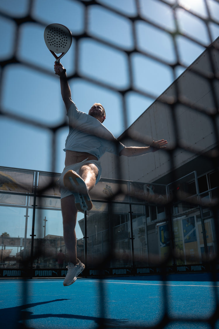 Player stretching for an overhead smash, seen through the netting
